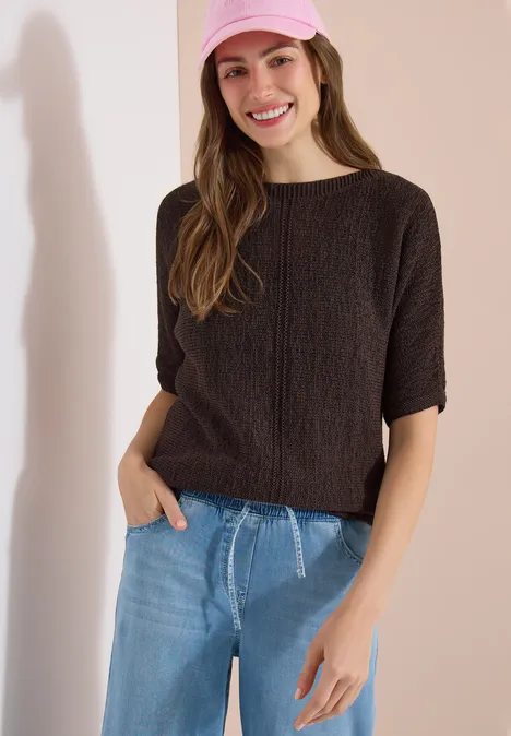 Dolman Pullover mit U-Boot-Ausschnitt brown cacao Frau mit kurzärmeligem, dunkelbraunem Zopfpullover und blauen Jeans, eine Hand lässig in der Tasche.