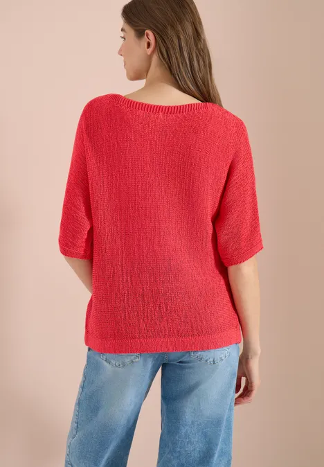 Vue de dos d’une femme portant un pull rouge ample à manches mi-longues et un jean bleu.