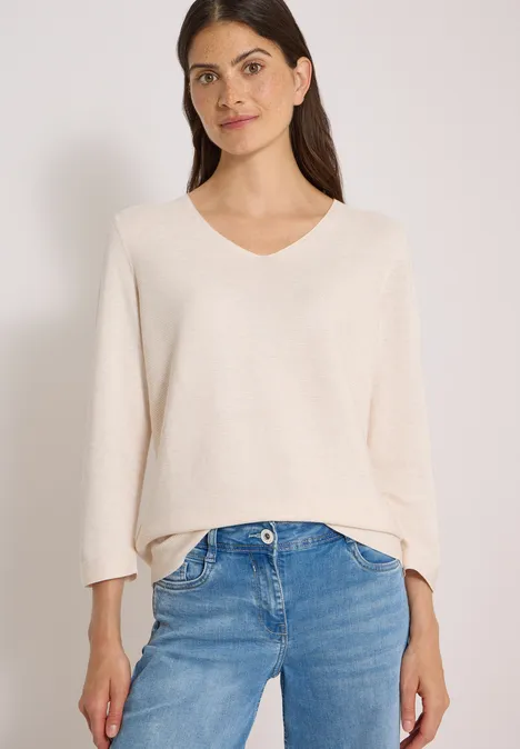 Frau in cremefarbenem V-Pullover mit V-Ausschnitt und lockeren blauen Jeans.
