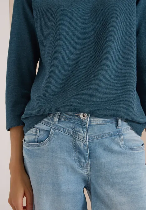 Person trägt ein dunkelgrünes Langarmshirt und helle Jeans.