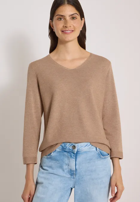 Frau in hellbraunem V-Pullover und blauen Jeans.