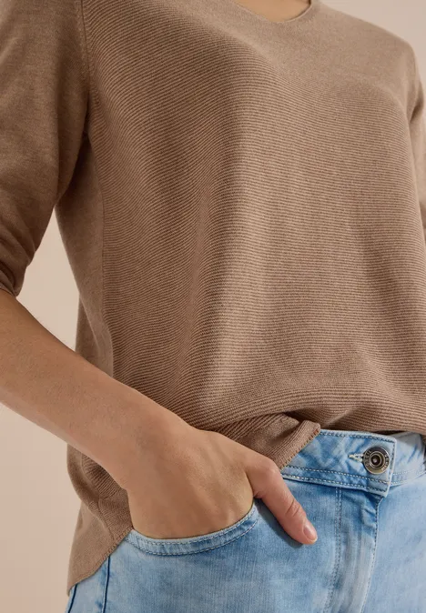 Frau in beigem Shirt steckt Hand in blaue Jeanshose