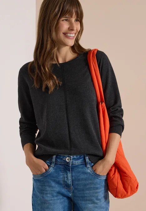 Femme souriante en pull gris et jean, portant un sac orange à l'épaule