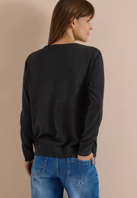 Femme de dos portant un pull noir et un jean bleu sur fond neutre.