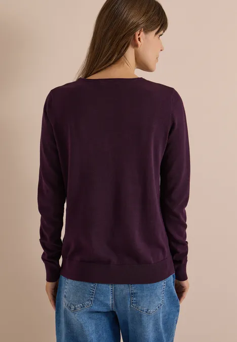 Femme vue de dos portant un pull violet et un jean sur fond neutre.