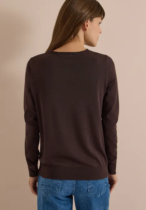 Personne de dos portant un pull marron et un jean bleu devant un fond neutre.
