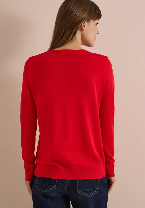 Vue de dos d’une femme portant un pull rouge sur fond beige clair.