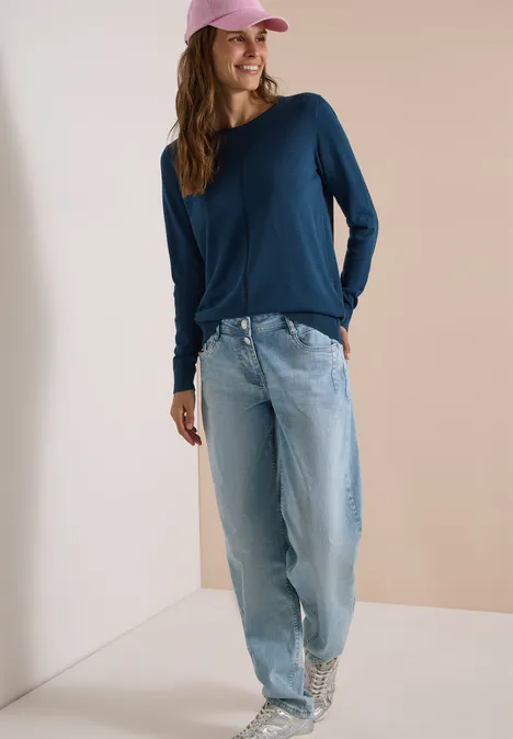 Basic Pullover mit Rundhals in Unifarbe moonlight blue Frau in lockeren hellen Jeans, dunkelblauem Langarmshirt, weißen gemusterten Sneakern und pinker Cap.