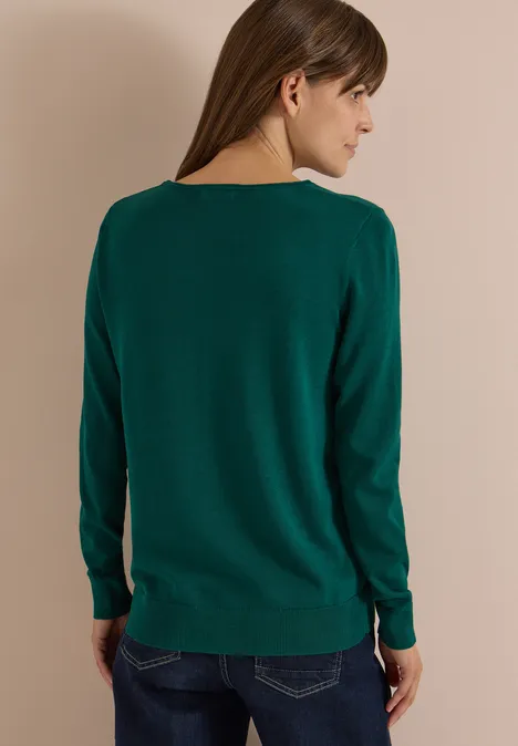 Femme de dos portant un pull vert foncé à manches longues.