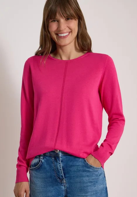 Basic Pullover mit Rundhals in Unifarbe pink flash Eine Frau trägt ein pinkes Langarm-Shirt und blaue Jeans und lächelt vor hellem Hintergrund.