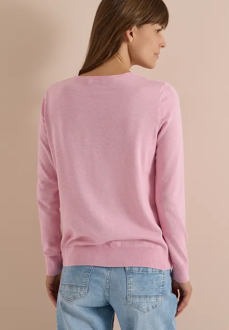 Femme vue de dos portant un pull rose et un jean sur fond beige.