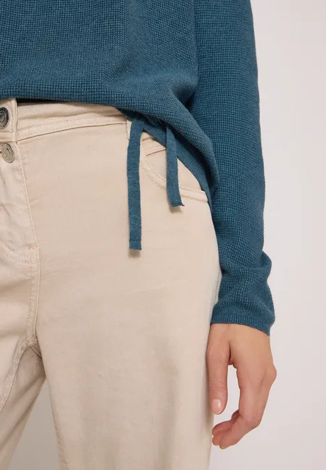 Pull à col rond et texturé dull teal blue melange Nahaufnahme einer Person in beigen Hosen und tealfarbenem Pullover mit Hand am Oberschenkel