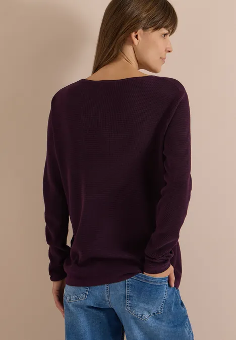 Frau von hinten, lila Pullover und Jeans vor neutralem Hintergrund.