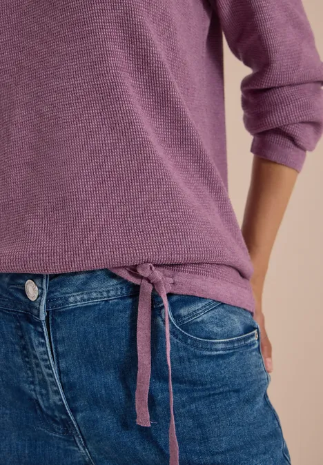 Gros plan sur un pull violet à cordon latéral et un jean bleu.
