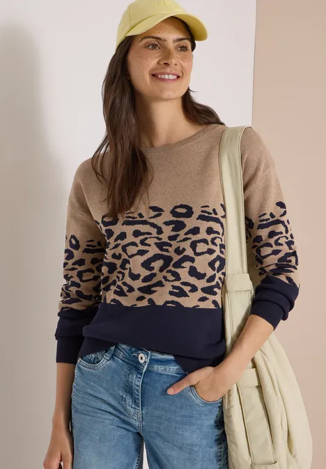 Langarm Pullover mit Leo-Jacquard-Muster urban dark blue Frau in beiger Kappe, Leoparden-Pullover und Jeans mit beiger Schultertasche vor hellem Hintergrund.