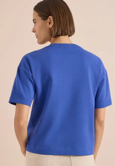 Bluza z krótkim rękawem z haftem deep river blue Kobieta widziana od tyłu ma na sobie niebieską bluzkę z krótkim rękawem.