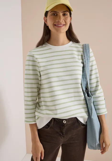 3/4-Arm Sweatshirt mit Rundhals und Streifen raw matcha lime Eine Frau trägt ein gestreiftes Shirt, Cap und Tasche, lächelt vor hellem Hintergrund.