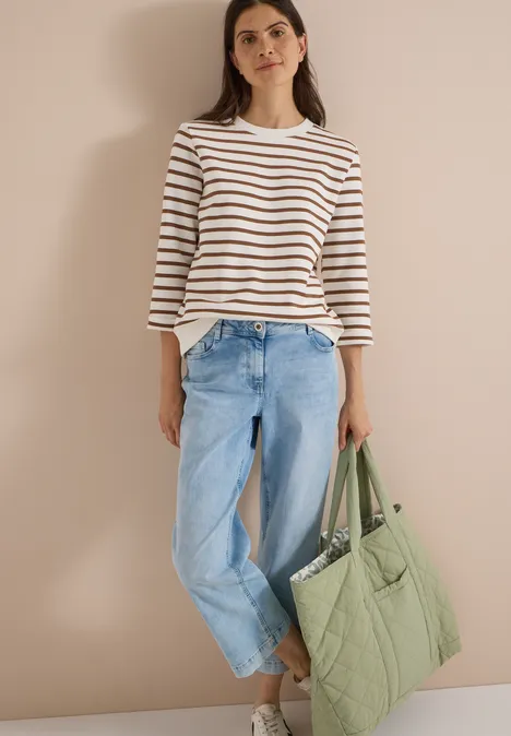 3/4-Arm Sweatshirt mit Rundhals und Streifen creamy mocha Frau mit weiß-blau gestreiftem Langarmshirt, hellblauen Jeans und großer grüner Stepp-Tasche vor neutralem Hintergrund.