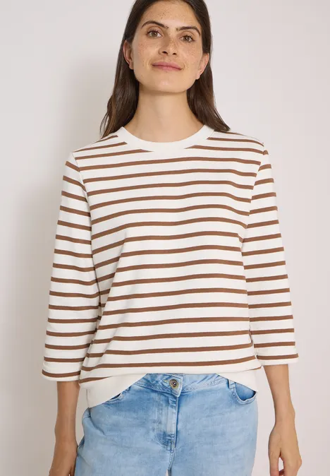 3/4-Arm Sweatshirt mit Rundhals und Streifen creamy mocha Frau in weiß-braun gestreiftem Shirt und blauen Jeans, frontal stehend, Haare offen, dezentes Lächeln.