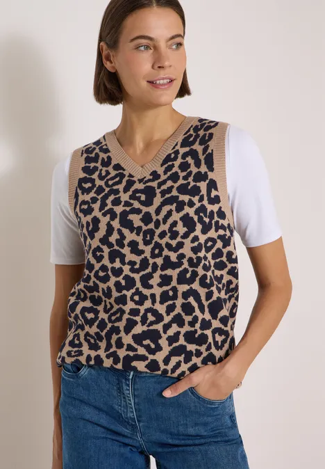 Frau in Jeans und ärmellosem Pullunder im Leopardenmuster über weißem T-Shirt.