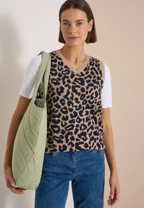 Frau mit Leopardenstrickweste über weißem T-Shirt, Jeans und gestepptem grünen Shopper an der Schulter.