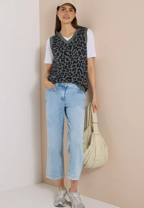 Frau trägt weiße Kappe, T-Shirt, Leoparden-Pulli, weite Jeans und Schultertasche, lässiger Look.