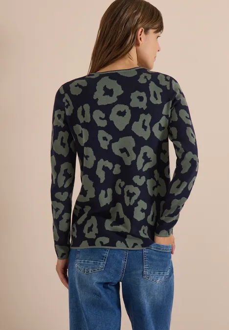 Vrouw van achteren met groen-zwarte luipaardtrui en blauwe spijkerbroek.