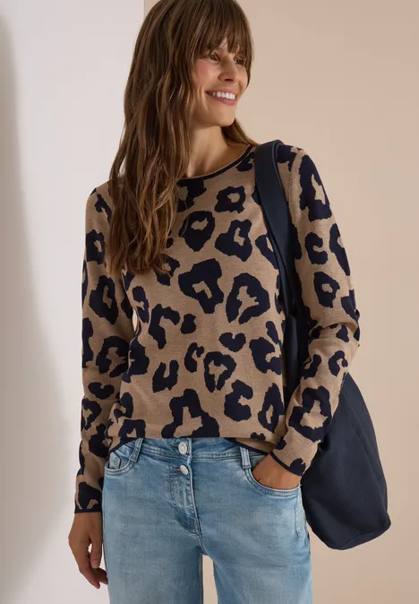 Vrouw lacht, draagt beige-zwart luipaardtrui, blauwe spijkerbroek en donkerblauwe tas.