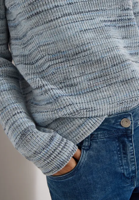 Personne porte un pull en tricot bleu clair et a la main dans la poche avant d'un jean bleu.