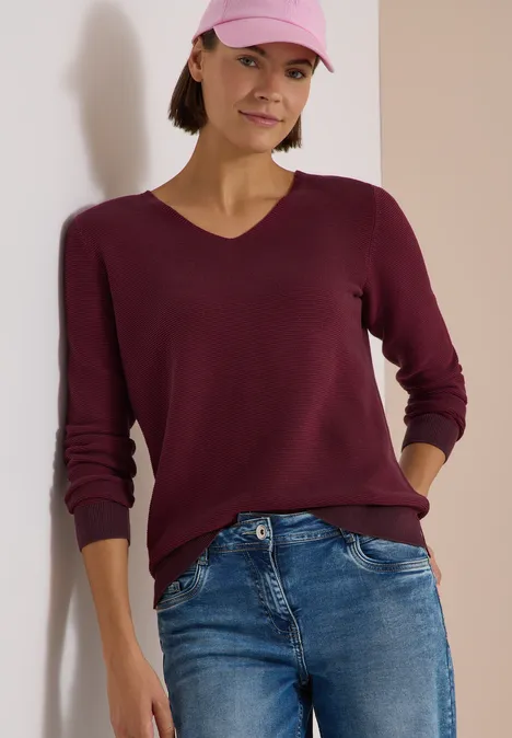 Frau in Jeans, burgunderfarbenem Pullover und rosa Kappe.