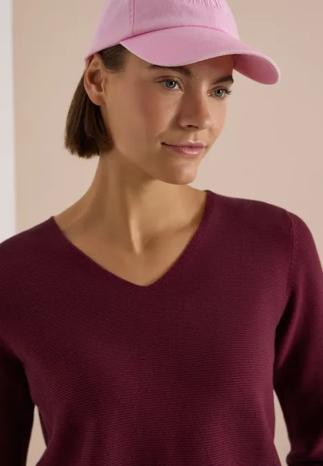 Frau trägt rosa Baseballcap und burgunderroten V-Pullover.