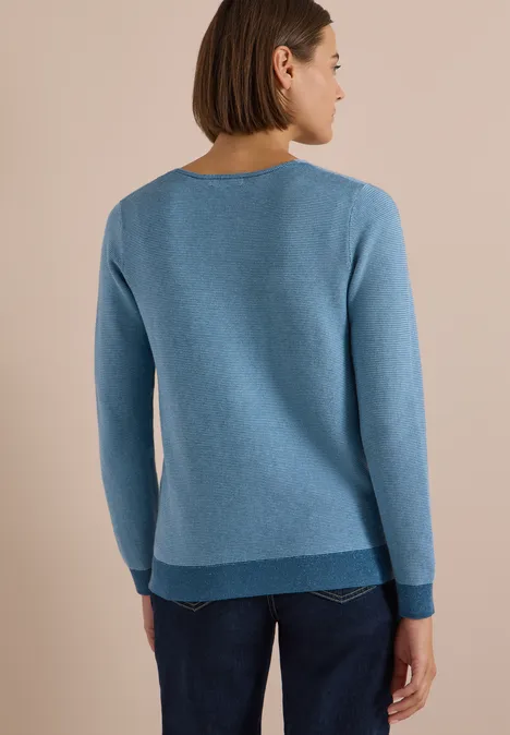 Rückenansicht einer Frau in hellblauem Pullover und Jeans vor beigem Hintergrund.