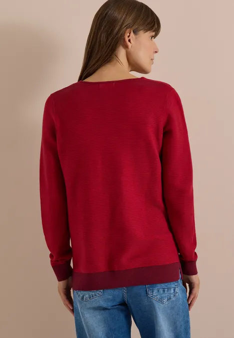 Frau von hinten in rotem Pullover und blauen Jeans.