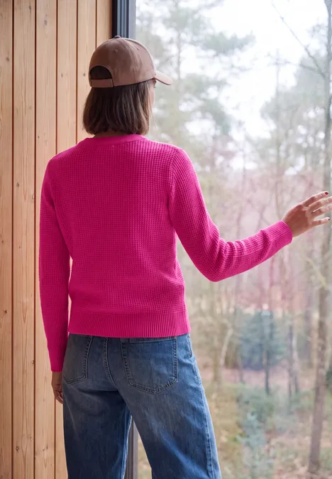 Persoon in roze trui en pet, van achteren gefotografeerd, kijkend via raam naar het bos.