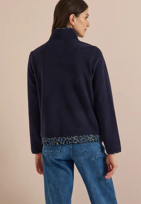 Vrouw van achteren in marineblauwe fleecetrui met luipaardprintbies en spijkerbroek, beige achtergrond