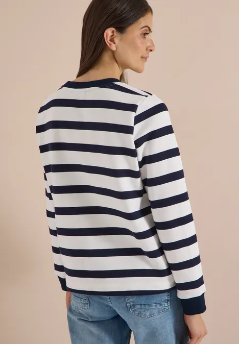 Rückenansicht einer Frau in weiß-blau gestreiftem Langarmshirt und hellblauen Jeans.