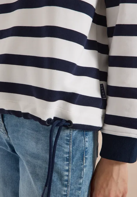 Person trägt blau-weißen Streifenpullover mit Kordelzug und Jeans.