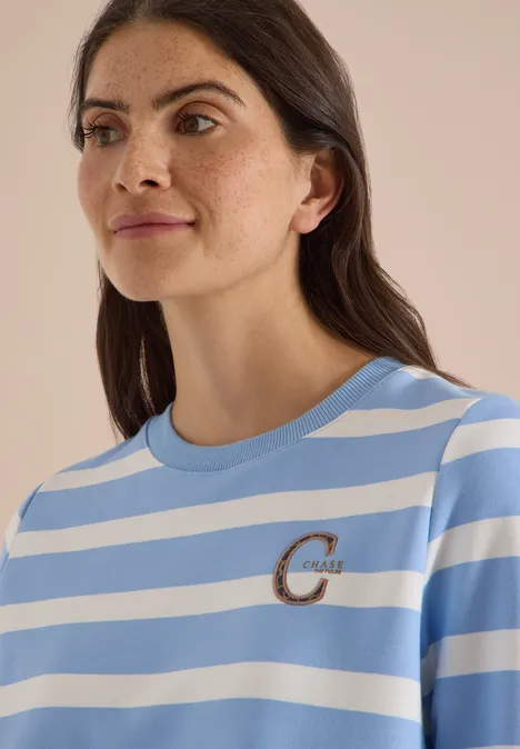 Frau trägt hellblau-weiß gestreiftes T-Shirt mit kleinem goldfarbenen 'C'-Logo auf der Brust.