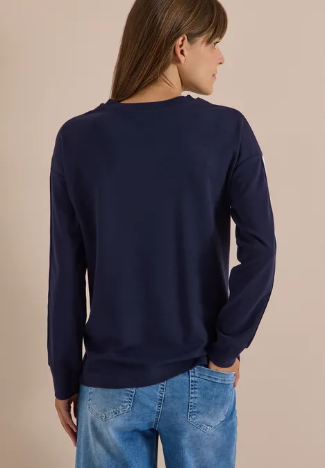 Sweatshirt met ronde hals en tape-details urban dark blue Vrouw van achter gezien, draagt een donkerblauw shirt met lange mouwen en blauwe spijkerbroek, handen in de zakken.