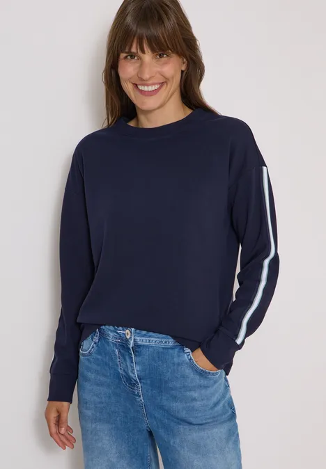 Sweatshirt met ronde hals en tape-details urban dark blue Vrouw met marineblauwe trui met witte streep op de mouw en jeans, glimlachend.