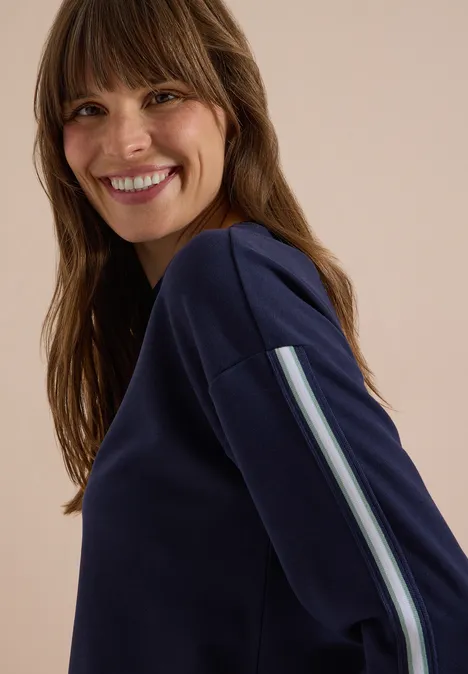 Sweatshirt met ronde hals en tape-details urban dark blue Een vrouw lacht in een blauw sweatshirt met een streep op de mouw, kijkend over haar schouder.