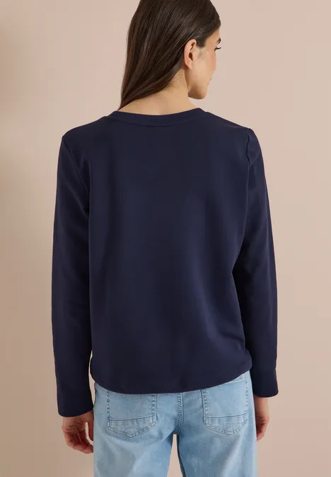 Eine Frau von hinten trägt ein dunkelblaues Langarmshirt und helle Jeans.