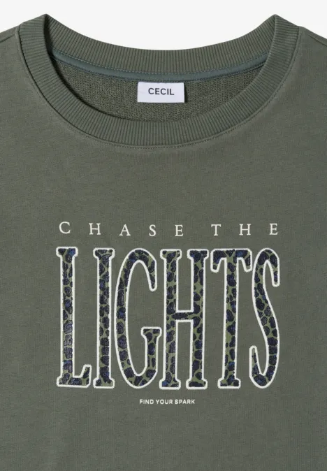 Olivegrünes T-Shirt mit Markenlabel und großer Aufschrift 'CHASE THE LIGHTS' in gemusterten Buchstaben.
