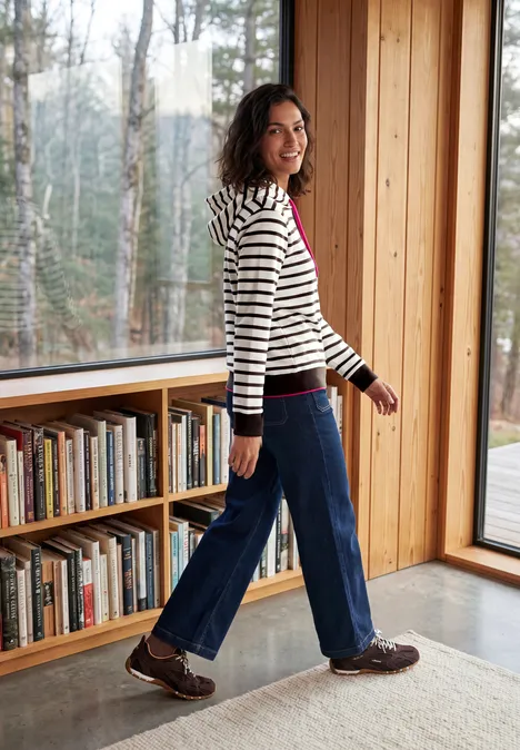 Sweatshirt mit Kapuze und Streifen truffle brown Eine Frau in gestreiftem Pullover läuft in einem hellen Raum mit Bücherregal und Panoramafenster.