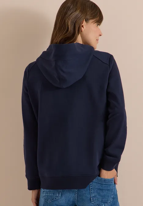 Persoon van achteren in een donkerblauwe hoodie en jeans voor een lichte achtergrond