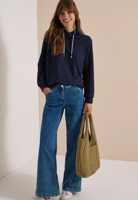 Vrouw in marineblauwe hoodie, wijde jeans en met grote olijfgroene shopper.