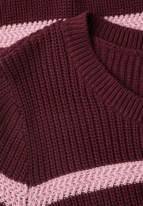 Close-up van een gebreide trui in bordeauxrood met roze horizontale strepen.