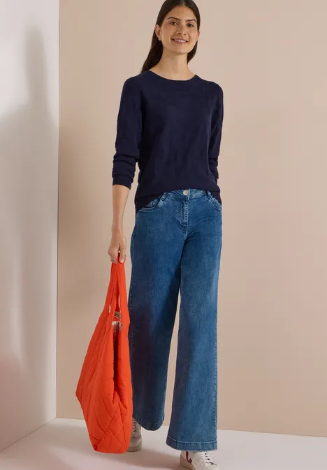 Pull à col bateau et texturé urban dark blue Frau trägt dunkelblauen Pullover, weite Jeans und hält eine rote Tasche.