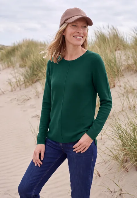 Langarm Pullover mit Rundhals und Struktur dark fir green Lächelnde Frau in grünem Pullover und Mütze steht am Strand vor Sanddünen.
