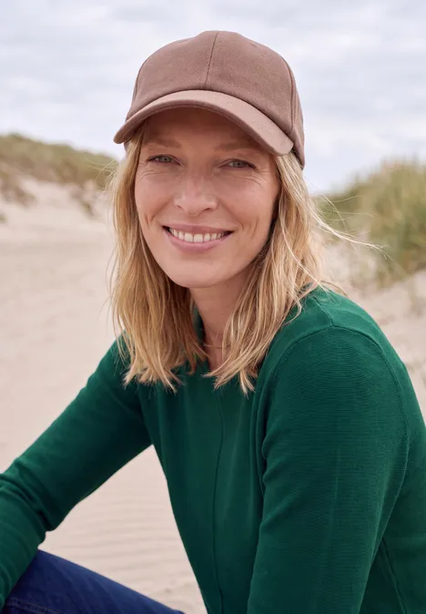 Langarm Pullover mit Rundhals und Struktur dark fir green Eine lächelnde Frau mit Baseballcap und grünem Pullover sitzt am Strand, im Hintergrund Sanddünen.